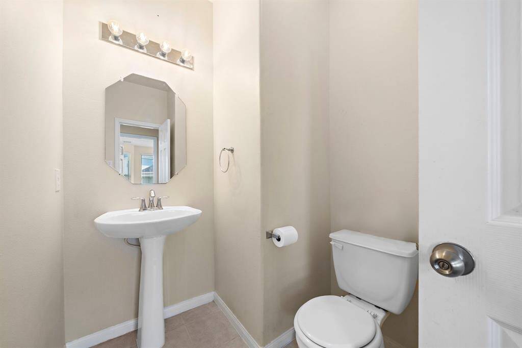 The powder room offers a clean and practical design with a pedestal sink and modern fixtures. Neutral tones create a fresh and inviting space, ideal for guests and quick access from main living areas.