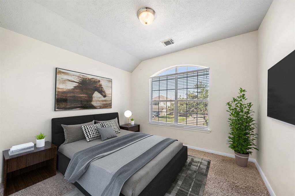 The secondary bedroom offers a peaceful retreat with plush carpeting and a large arched window that bathes the space in natural light. Neutral tones and elegant decor provide a modern and welcoming ambiance, ideal for rest and relaxation.