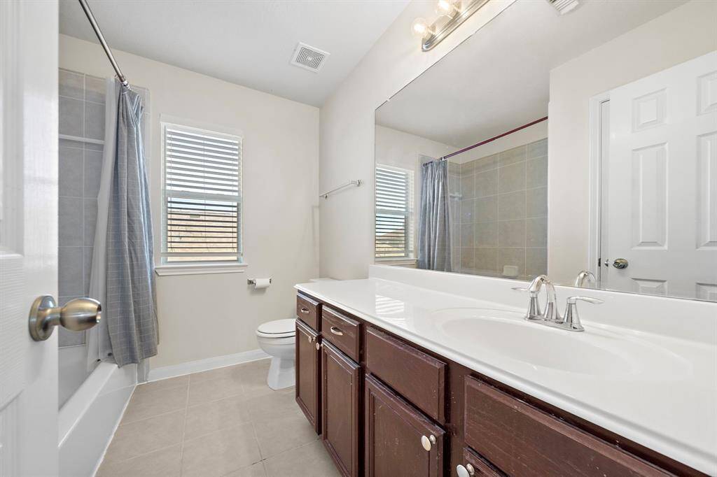 The secondary bathroom offers a clean and bright ambiance with a spacious vanity providing ample countertop space. The tiled shower and bathtub combo, along with the large mirror and natural light streaming through the window, create a functional and inviting space for daily routines.