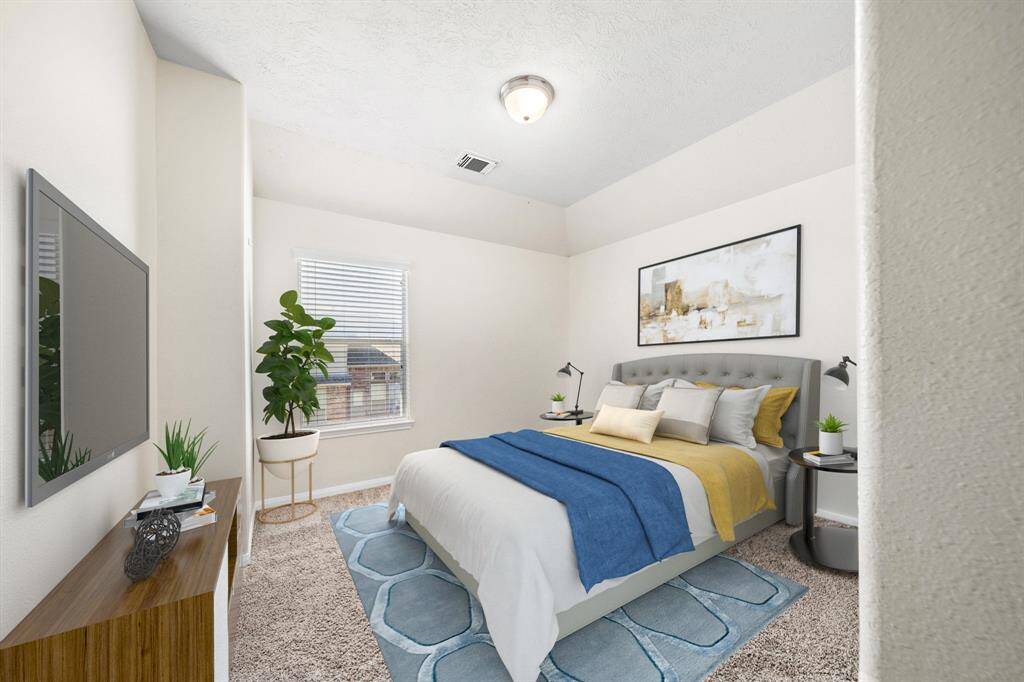 The secondary bedroom is a tranquil space, featuring plush carpeting and ample natural light through a large window. Neutral tones and modern decor create a warm, inviting atmosphere, ideal for relaxation. Elegant touches, such as carefully chosen furnishings and artwork, complete this serene retreat.