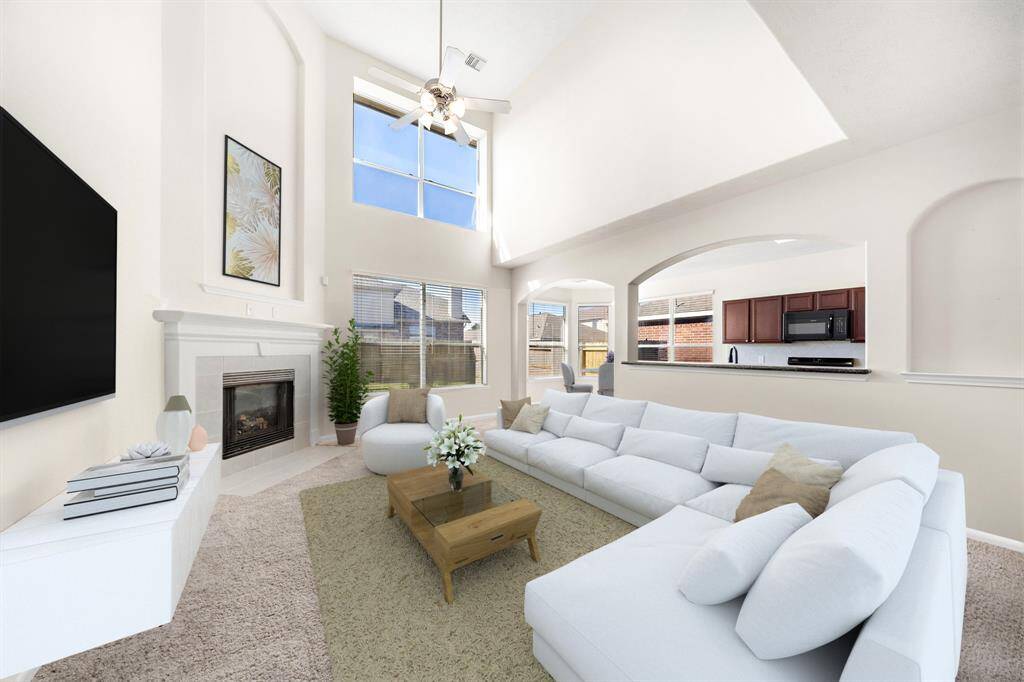 The open-concept living room exudes warmth with a cozy fireplace and high ceilings. Expansive windows flood the space with natural light, while built-in shelving offers practical storage. Enjoy seamless flow to the kitchen and dining area, perfect for entertaining. This photo has been virtually staged.