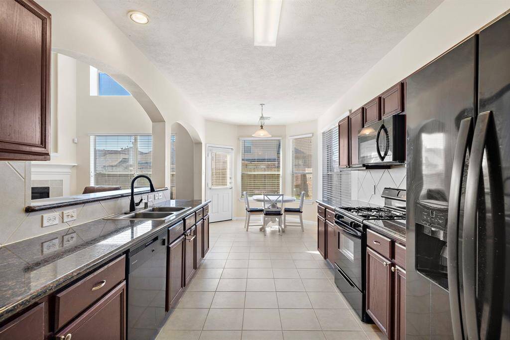 The kitchen, showcasing a sleek design, is equipped with stainless steel appliances and granite countertops. Enjoy the convenience of a gas range and a spacious walk-in pantry, while natural light streams through expansive windows highlighting the breakfast bar and dining area access.