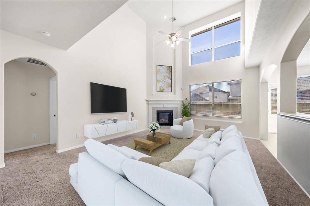 The inviting living room features plush carpeting and a cozy fireplace, perfect for relaxation. Expansive windows allow natural light to illuminate the space, highlighting the open layout that seamlessly connects to nearby areas. Ideal for gatherings, the high ceilings enhance the airy ambiance, while built-in shelving provides additional storage and decorative options. This photo has been virtually staged.