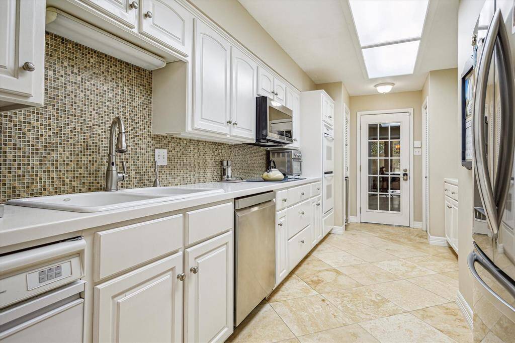The kitchen features an oversized sink, Corian countertops, stylish tile backsplash, and a travertine tile floor. The kitchen also has access to the garage!