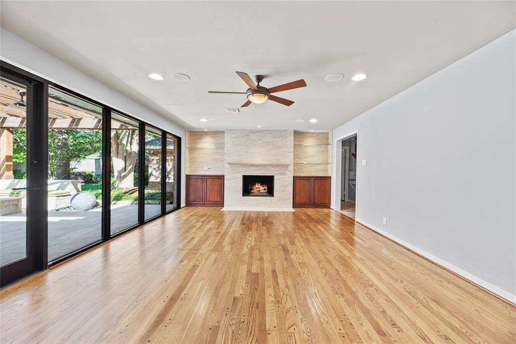 Classically remodeled den with sleek fireplace, built-in cabinetry, and floor-to-ceiling glass windows offering unobstructed views of the stunning backyard oasis.