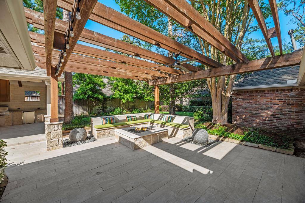 A resort-style backyard featuring a custom pergola, cozy wraparound stone seating with vibrant cushions, and a stone fire pit offering tranquil sounds of water features - perfect for relaxing or entertaining.