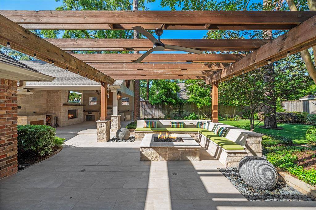 A continuation of the backyard retreat, highlighting the outdoor kitchen with built-in grill and fridge, fireplace, and seamless connection to the patio lounge area and showcasing two uniquely carved granite water features.