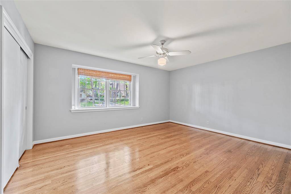 Spacious secondary bedroom with hardwood floors, neutral paint, and a large window that overlooks the beautifully landscaped front yard.