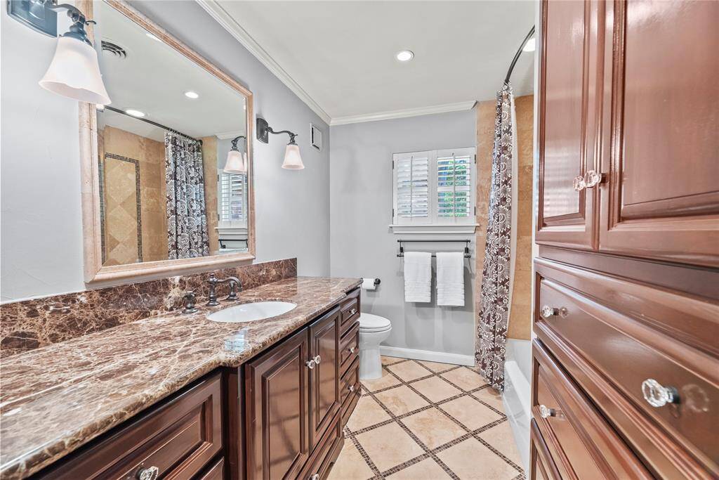 Elegant 1st floor guest bathroom remodeled with rich wood cabinetry, marble countertops, and a full shower/tub combo adorned with decorative tile detailing.