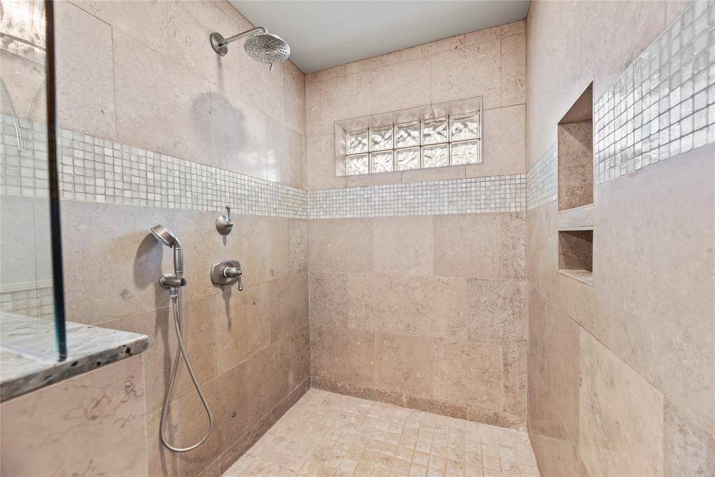 Highlighting the extended walk-in shower with custom tilework, dual showerheads, and built-in niches.
