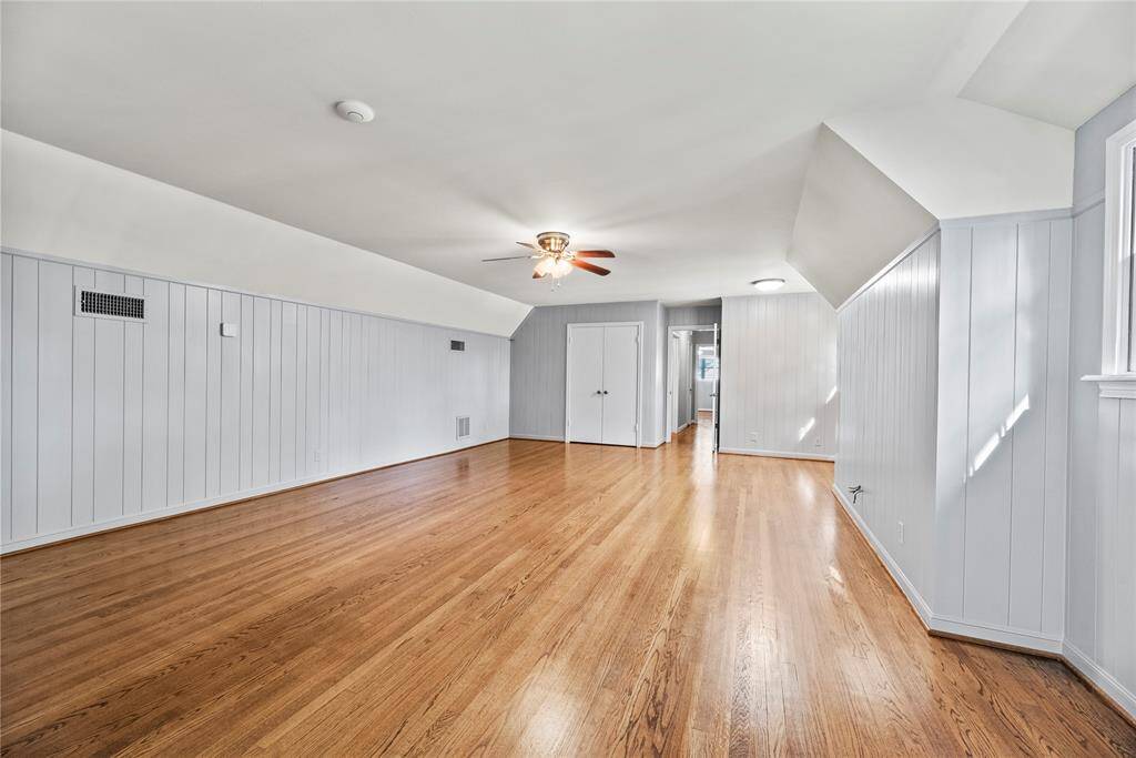 Expansive upstairs flex space with warm hardwood floors and crisp white paneling—perfect as a game room, media room, home gym, or even a spacious guest retreat. Natural light and charming ceiling angles add to its character and versatility.