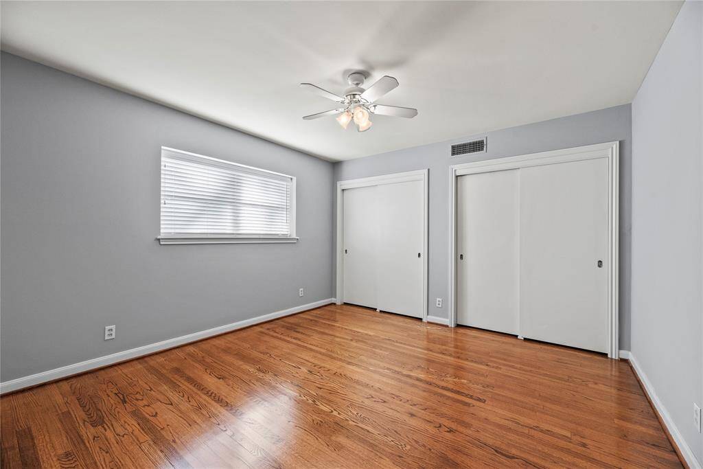 Spacious upstairs bedroom filled with natural light, featuring hardwood floors, soft gray walls, and a ceiling fan for added comfort.
