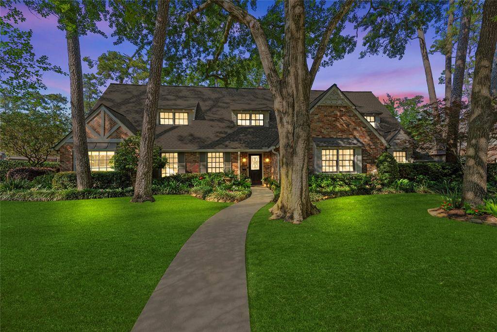 The home glows warmly under the evening sky, with soft exterior lighting enhancing the mature trees, inviting entry path, and timeless brick design.