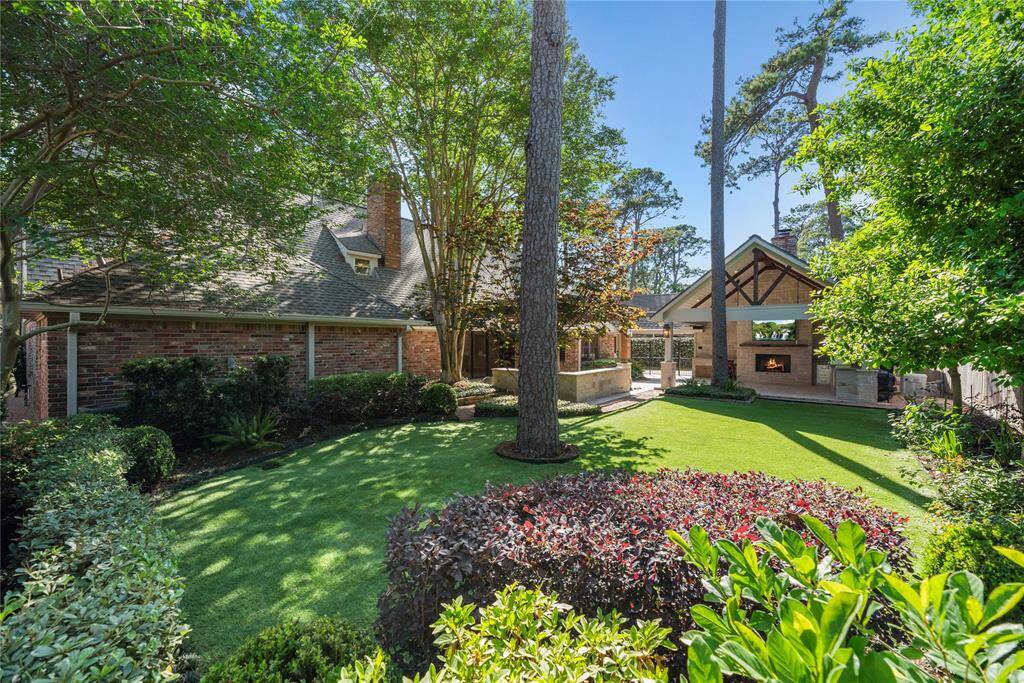 Lush side yard with neat landscaping and a view extending toward the outdoor kitchen and covered entertaining space.