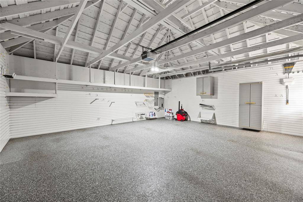 Immaculate garage with custom GarageTek slat wall panels for durable organization, sleek epoxy-coated floor, and exposed rafters for added character and vertical storage potential. A perfect blend of form and function for your tools, gear, or hobby space.