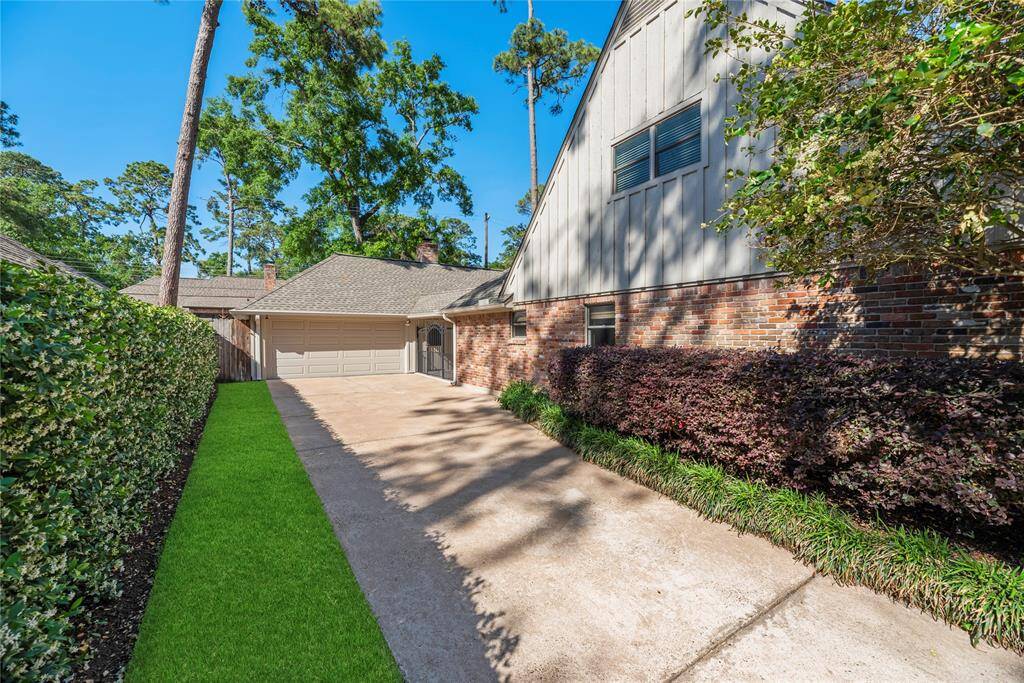 A wall of blooming jasmine leads you down the long driveway toward the detached garage, with the home’s classic architecture, well-kept yard, and mature trees on full display.