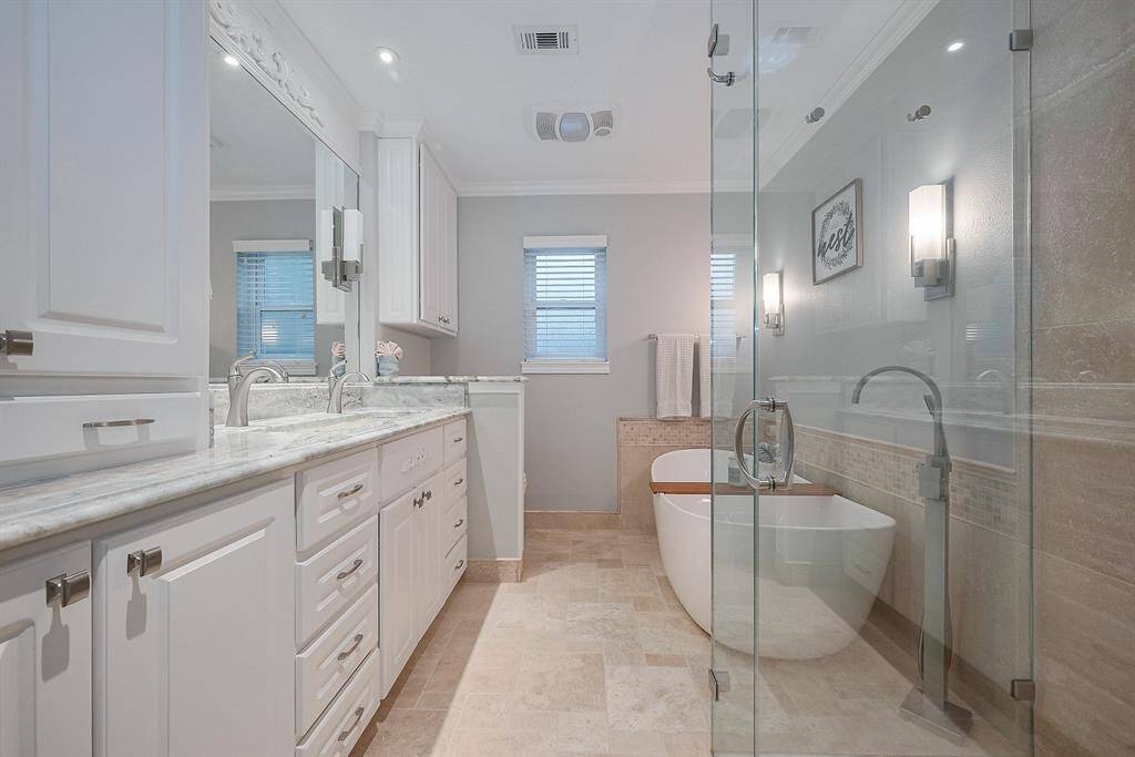 Stunning primary bathroom features a large soaking tub, granite counters, travertine tile and seamless shower.