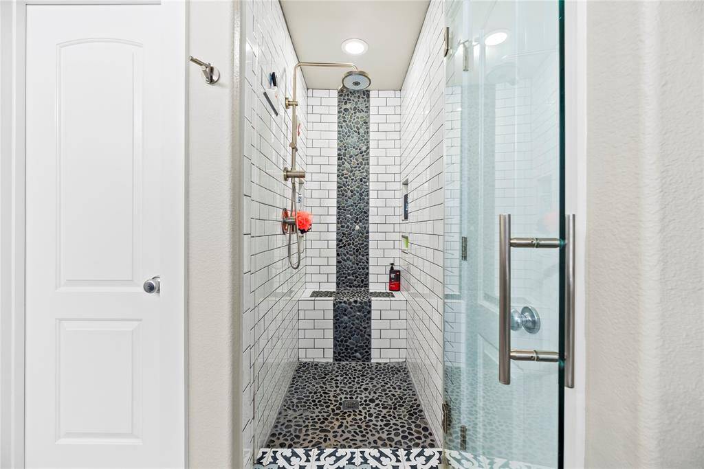 This photo showcases a walk-in shower with subway tiles and pebble flooring. It features a glass door, a rainfall showerhead, and built-in shelving, creating a sleek and functional bathing space. It is larger in person and will surely impress!