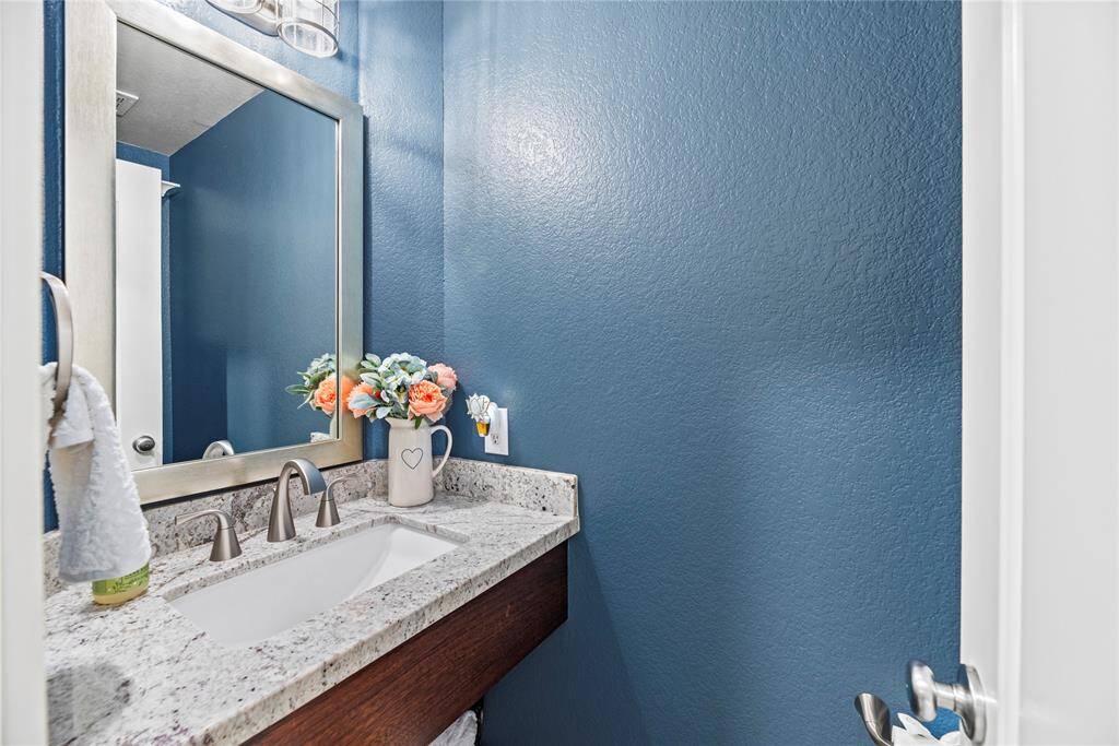 This photo showcases a stylish half bathroom with a granite countertop and beautiful built in sink and updated lighting.