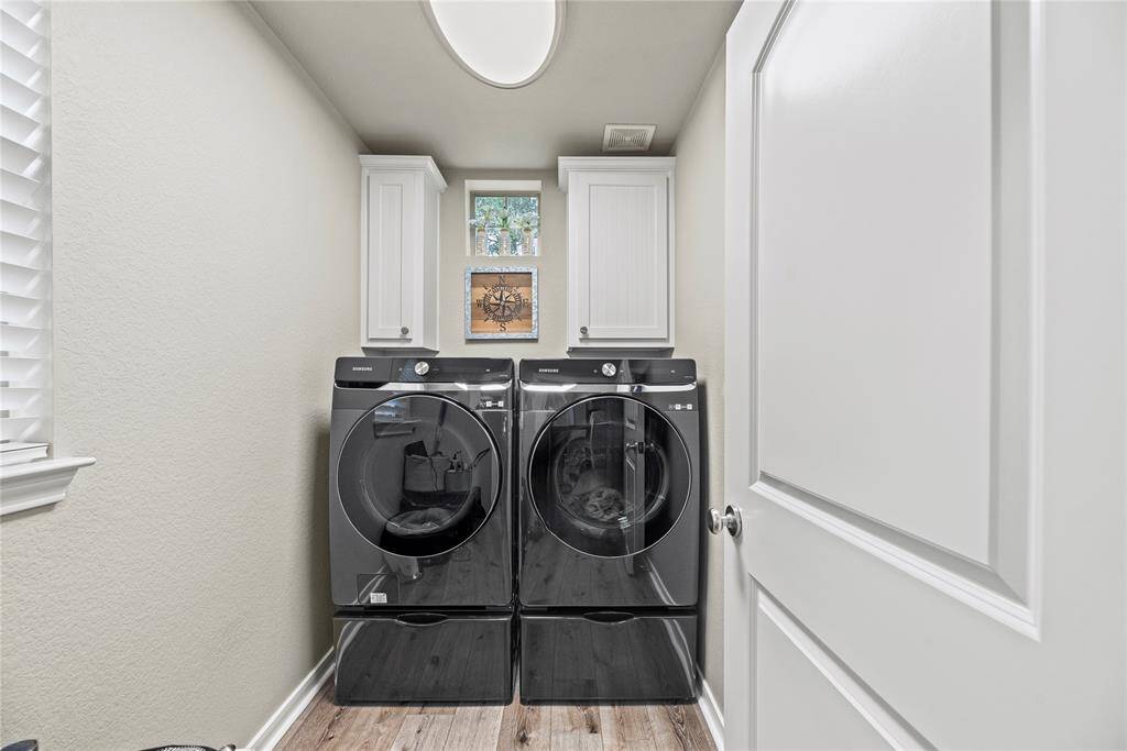 This laundry room features room for washer and dryer flanked by white cabinetry for storage. The space is well-lit with two windows and LPV flooring.