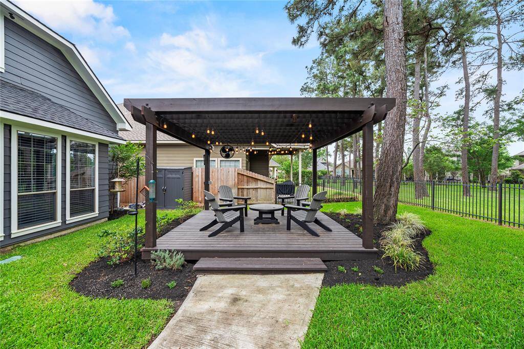 This photo showcases a charming backyard with a cozy pergola, perfect for outdoor relaxation. The space features a wooden deck with comfortable seating, surrounded by a well-maintained lawn and mature trees, creating a serene and inviting atmosphere.