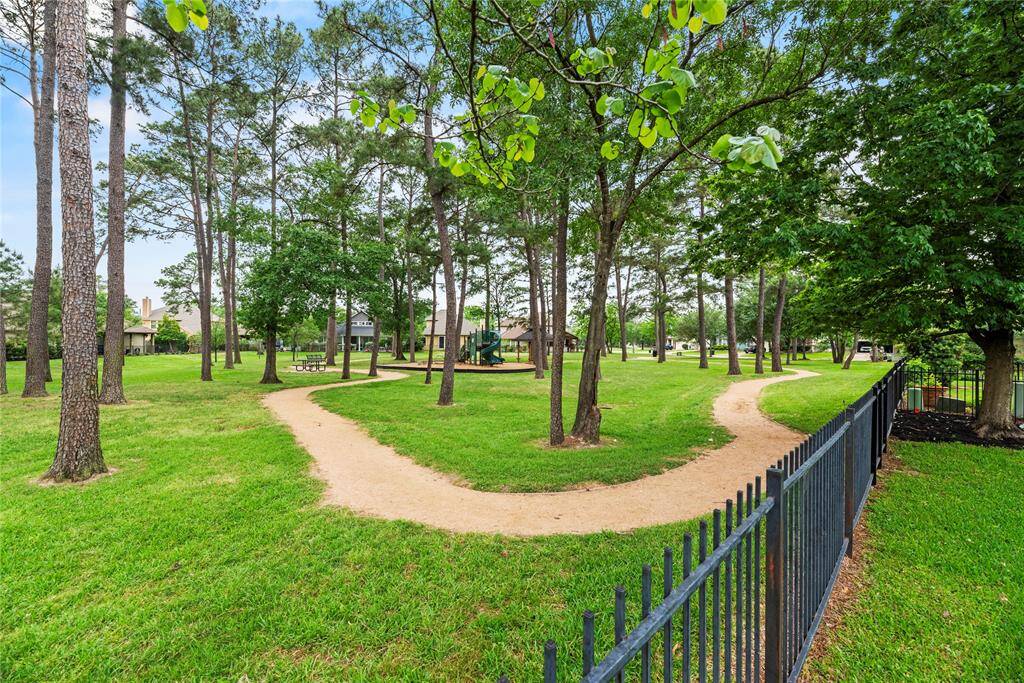 This photo showcases a serene neighborhood park with lush green grass, tall trees, winding walking paths, and a fenced perimeter. It's perfect for outdoor activities and relaxation.