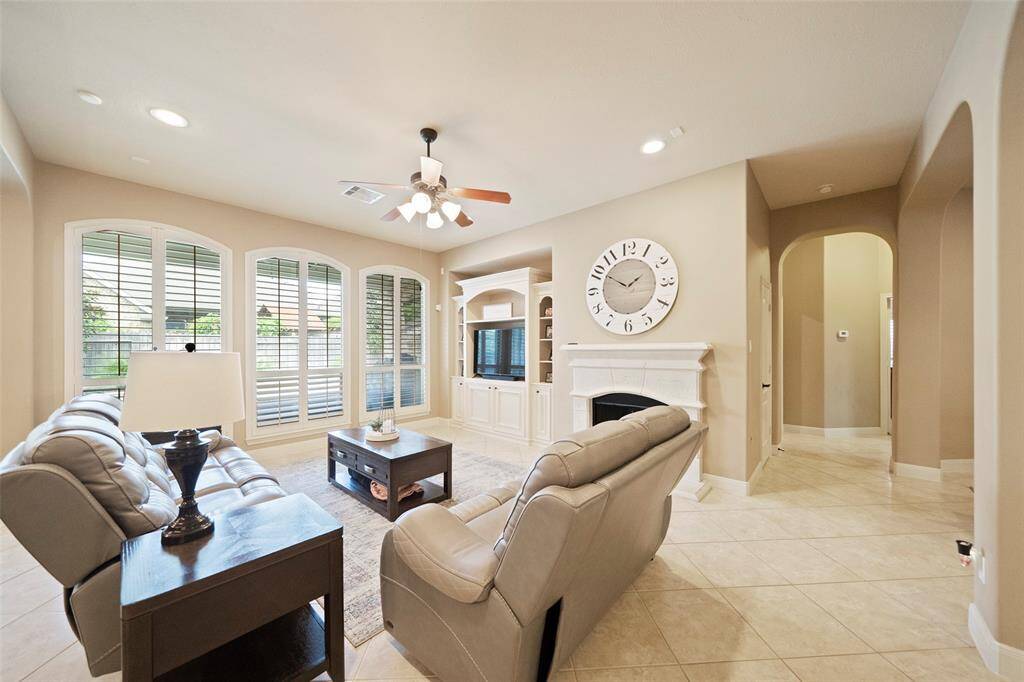 The spacious living room is anchored by a beautiful fireplace with custom built-ins, oversized windows with plantation shutters, and tile flooring for easy living.