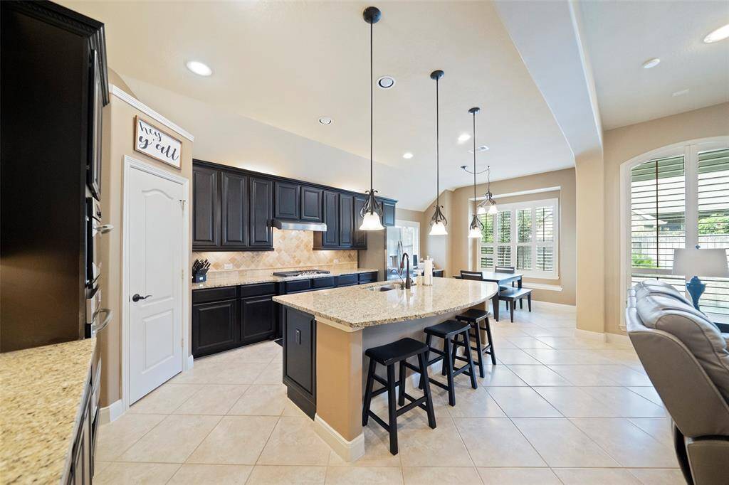 Chef’s dream kitchen features rich dark cabinetry, granite countertops, a gas cooktop, and a large center island with pendant lighting and breakfast bar seating.