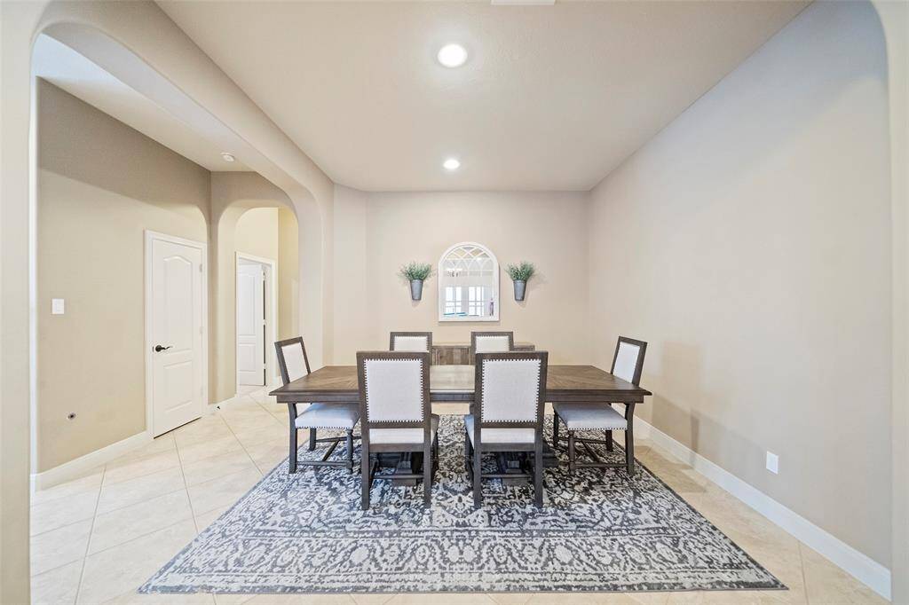 The formal dining room boasts graceful arched entries and recessed lighting, offering a spacious setting for entertaining with sophisticated tile flooring underfoot.