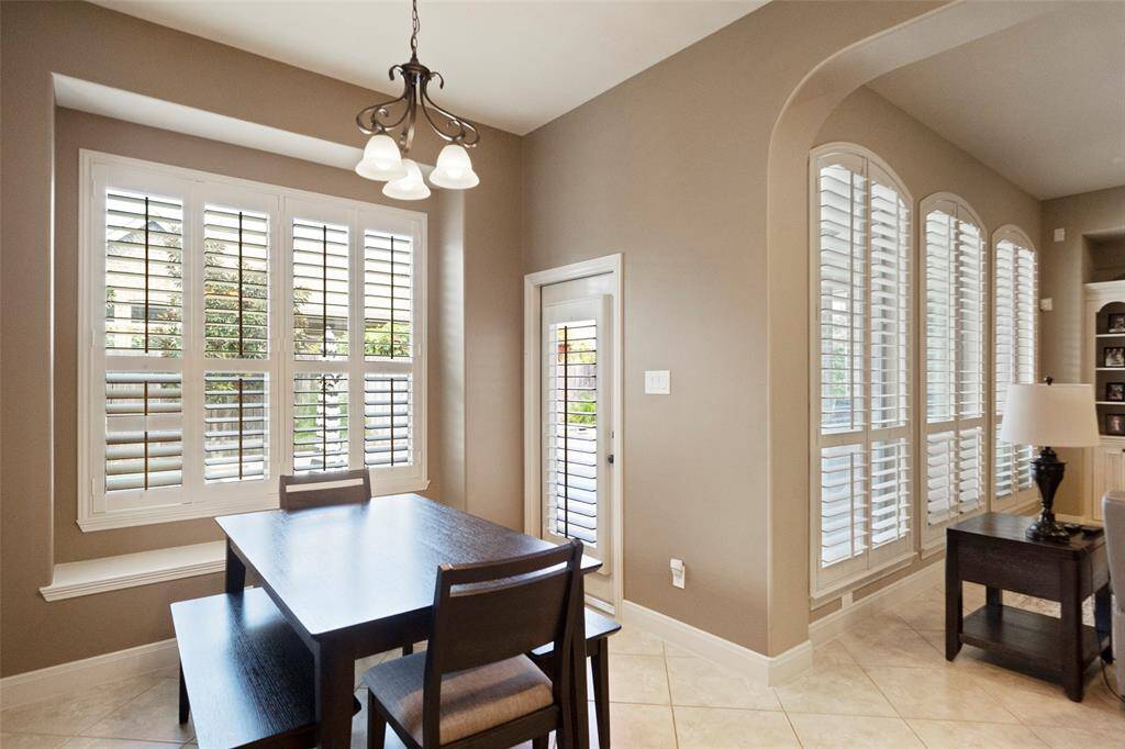 Bright and inviting breakfast nook featuring large windows with plantation shutters, providing serene views of the backyard. The space is enhanced by a classic light fixture and neutral tile flooring, perfect for morning coffee or casual dining.