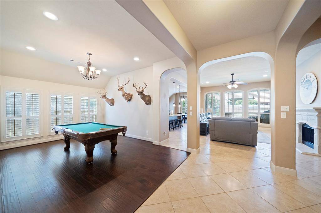 This expansive open-concept layout seamlessly connects the game room and living area, with wood floors, custom plantation shutters, and arched entryways enhancing the space.