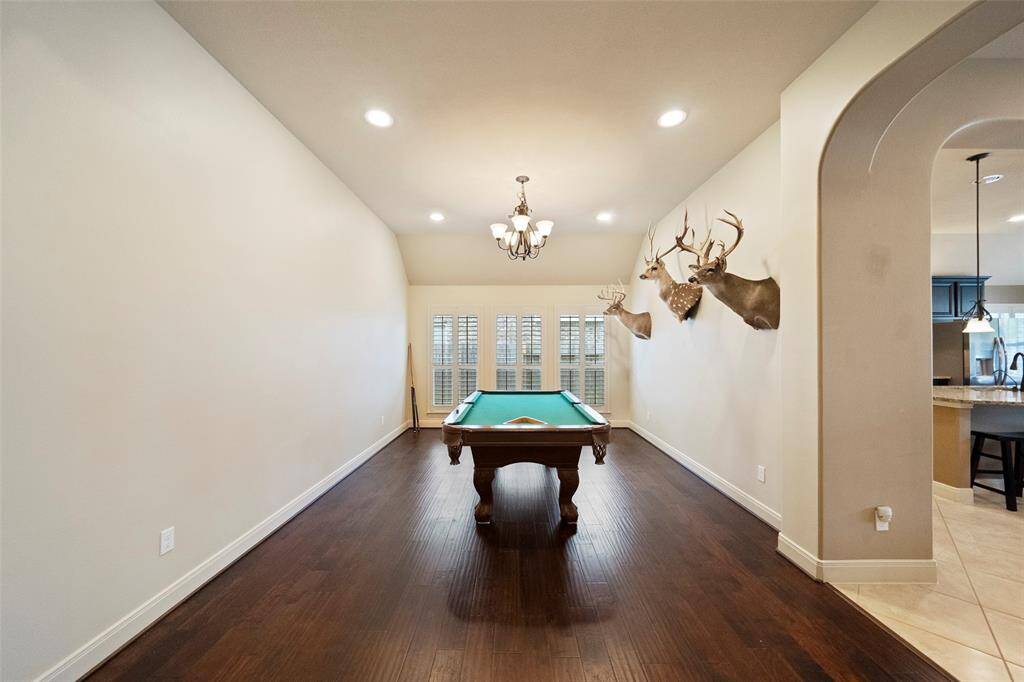 Enjoy quality time in the dedicated game room, complete with hardwood flooring, recessed lighting, and plantation shutters that fill the space with natural light.