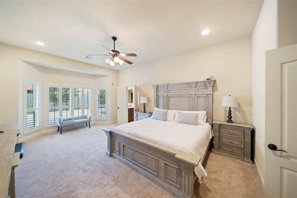 Luxurious primary bedroom retreat with tray ceiling, bay window seating area, and soft carpeted flooring. Ample space and natural light make this a peaceful escape.