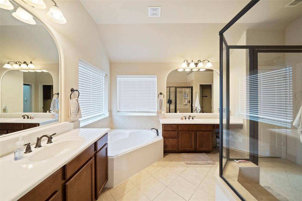 Relax in your spa-inspired bathroom featuring dual vanities, a soaking tub, separate walk-in shower, and warm wood cabinetry. Plenty of light and space to unwind in style.