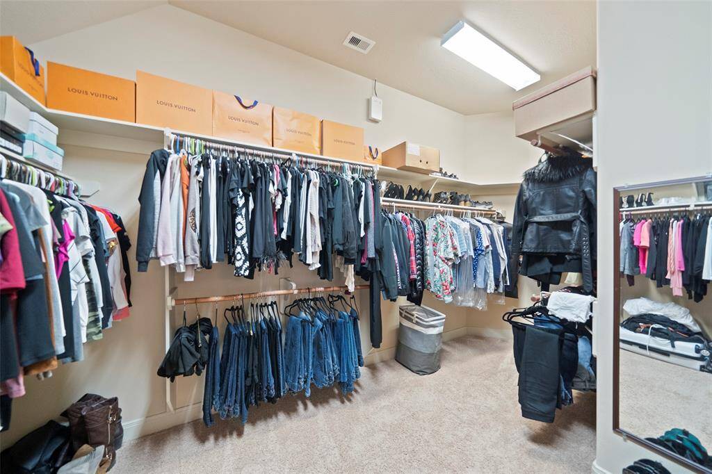 Impressive walk-in closet with built-in shelving and extensive hanging space, perfect for organizing wardrobes of any size. Plush carpet and overhead lighting complete the space.