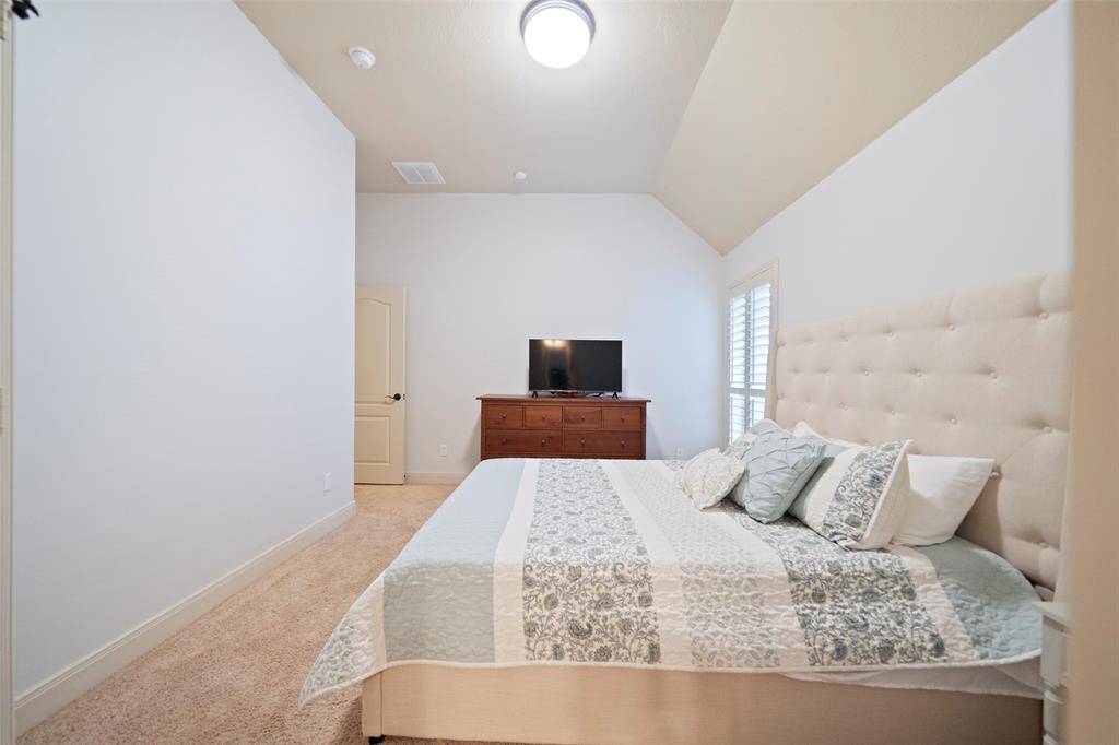 Bright and peaceful guest bedroom with high ceilings, soft carpeting, and a large window with plantation shutters. Ample space for a king-size bed and dresser, making it perfect for relaxation or hosting guests.