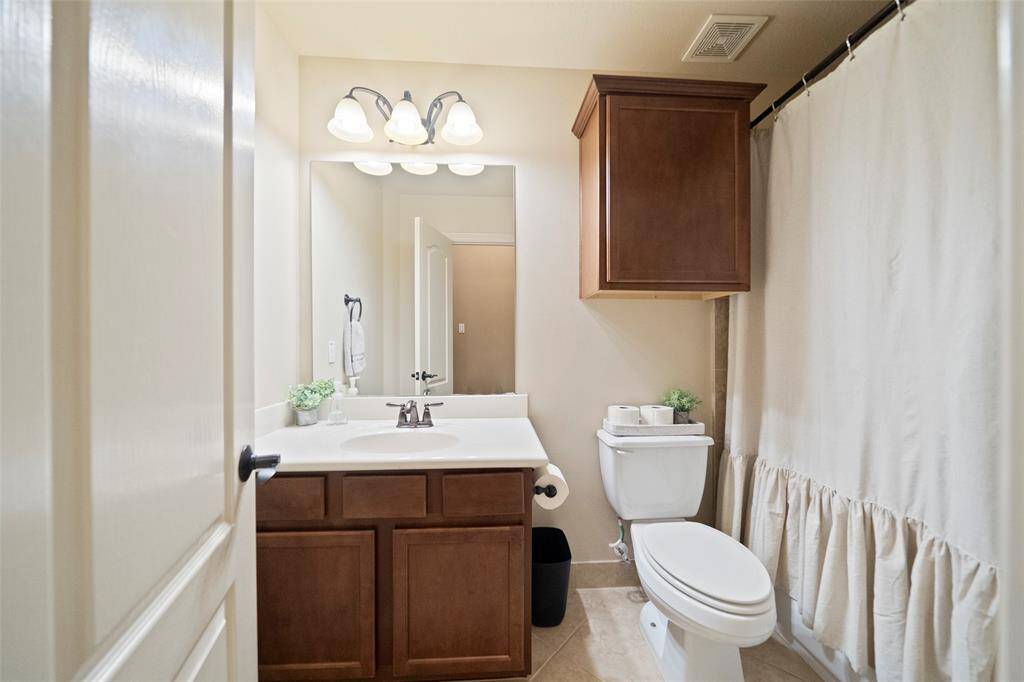 Well-appointed full bathroom offers a clean, classic design with wood cabinetry, brushed bronze fixtures, and a shower/tub combo with neutral tile surround.