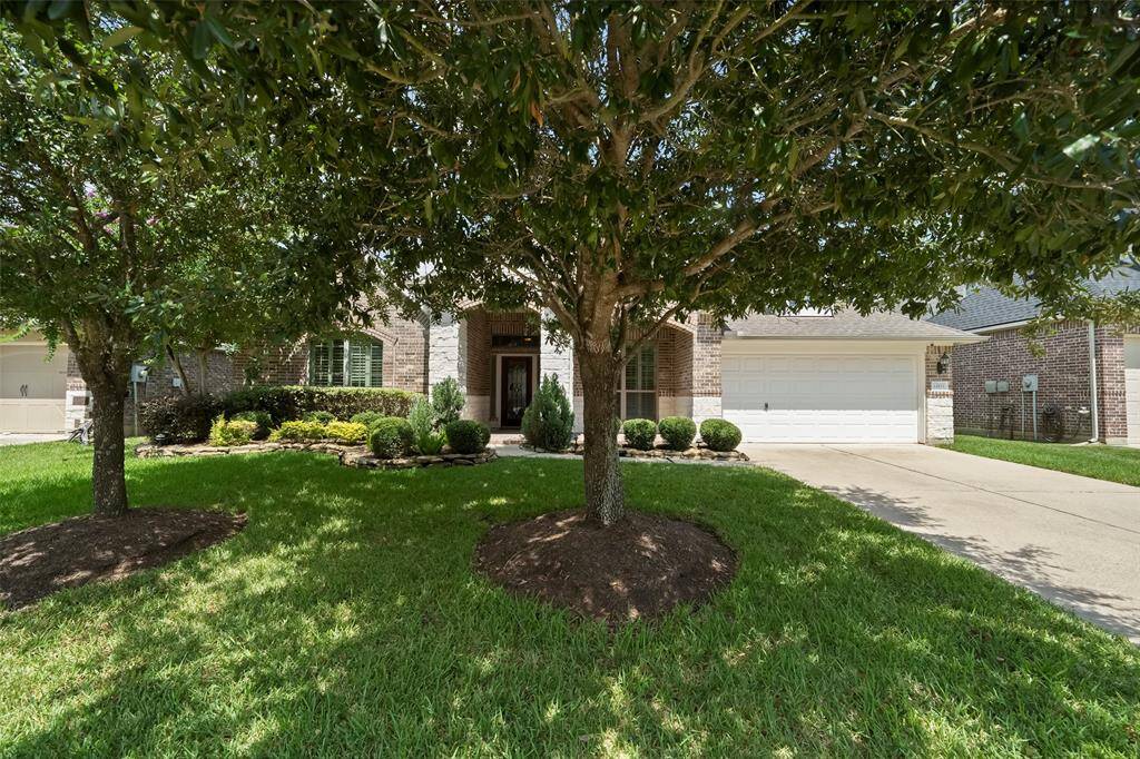 View of the home framed by lush mature trees providing shade and privacy, with a beautifully manicured lawn and vibrant front garden beds adding warmth and charm to the entrance.