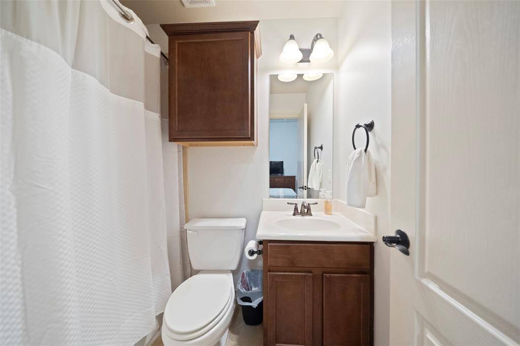 Charming full bathroom featuring a sleek vanity with storage, framed mirror, and overhead lighting. Includes a shower/tub combo with a crisp white curtain, complemented by neutral tones and bronze fixtures.
