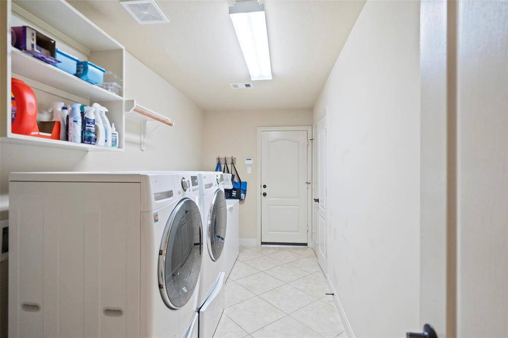 Oversized utility room for front-loading washer and dryer, built-in shelving, and tile flooring. A practical and tidy space for all your laundry needs.