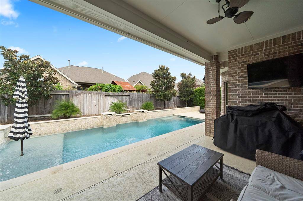 Spacious covered patio equipped with a ceiling fan, mounted TV, and seating area—ideal for outdoor entertaining. Overlooks the sparkling pool and offers seamless indoor-outdoor living.