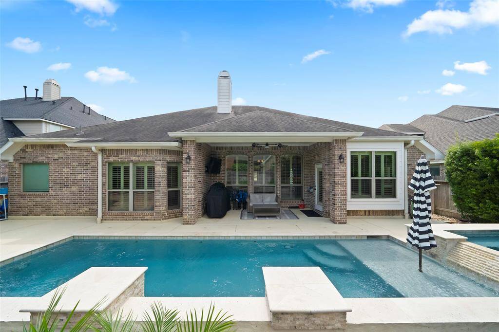 Gorgeous view of the home's full brick exterior and expansive backyard retreat. The pool and spa are perfectly positioned for relaxation, framed by manicured greenery and outdoor seating.