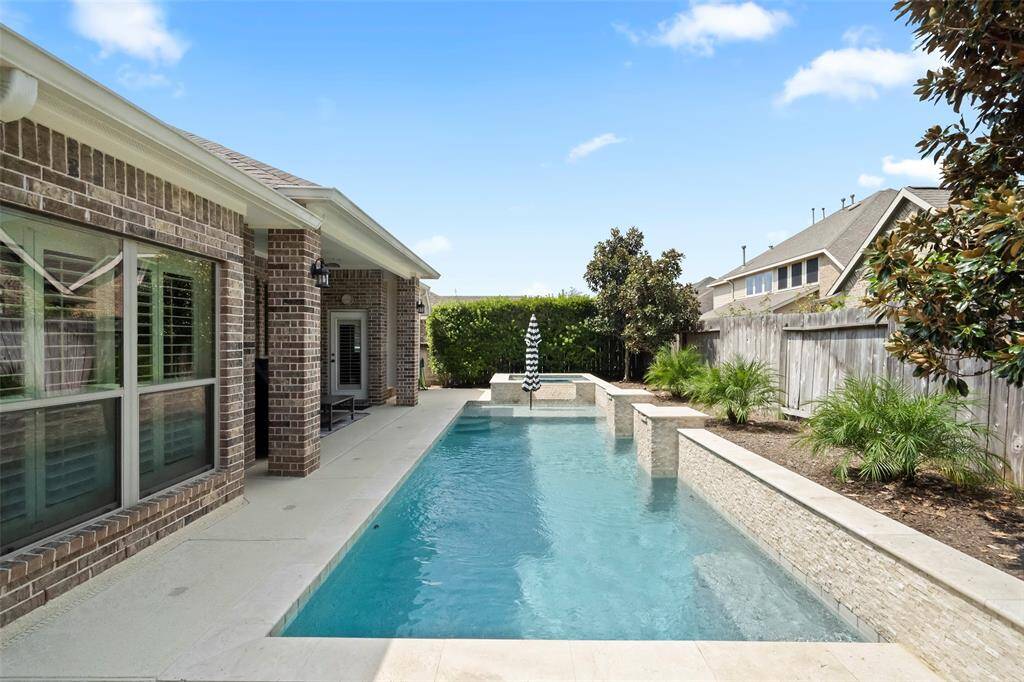 Impressive full rear elevation showcasing the extended covered patio, multiple windows with plantation shutters, and the stunning pool design with water features.