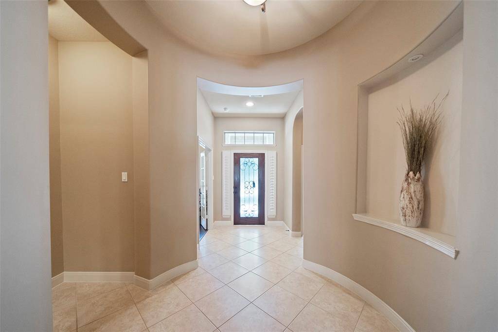 Welcome guests into an impressive rotunda-style entryway featuring soaring ceilings, elegant architectural curves, and neutral tile flooring that flows throughout the home.