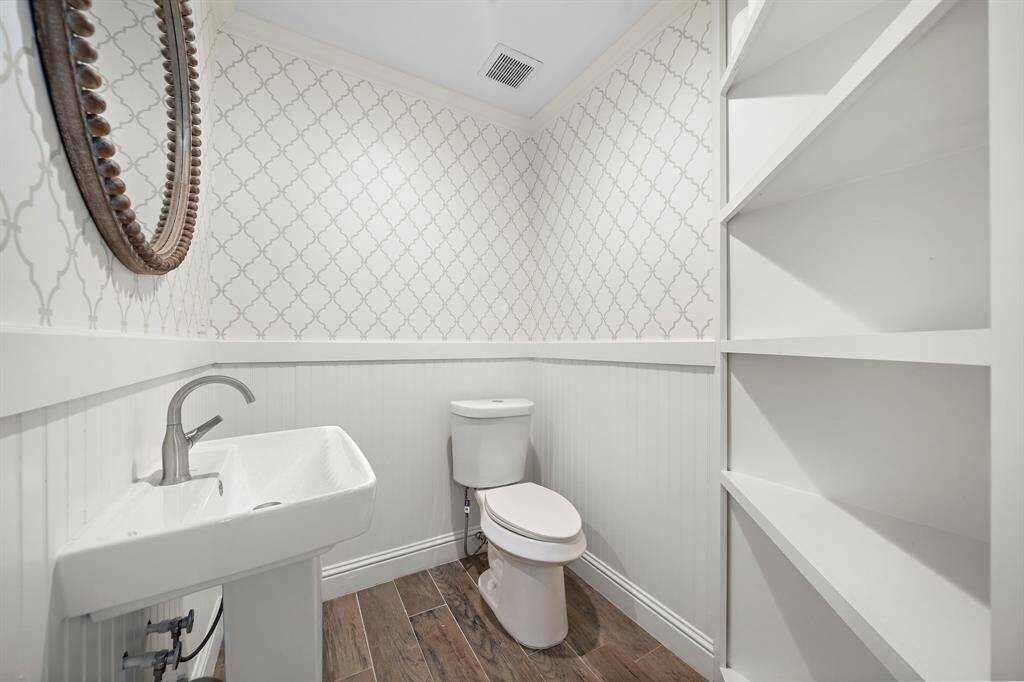 Elegant powder room featuring built-in cabinetry, stylish wallpaper, and a decorative mirror.