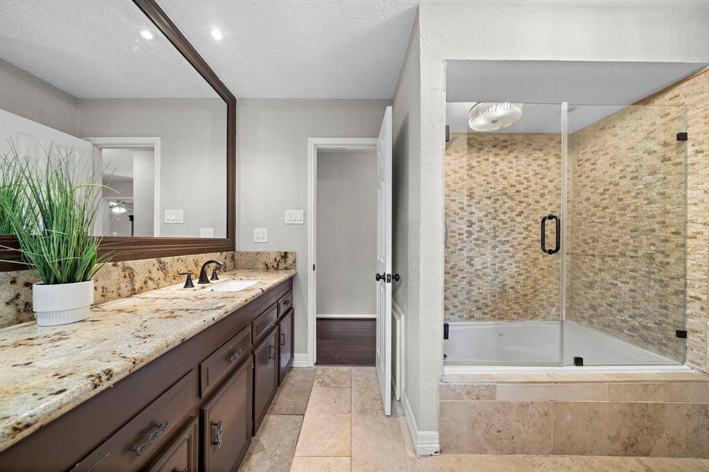 The guest bathroom features a spacious granite countertop and a jetted tub with a sleek frameless glass shower door.