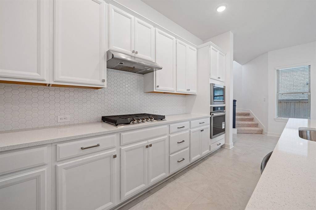 The kitchen boasts sleek white glass countertops paired with spacious white cabinets offering ample storage for all your needs.