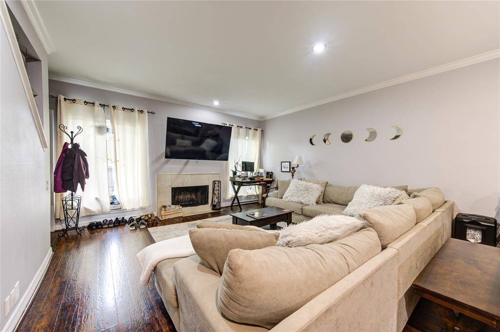 A cozy fireplace adds warmth, and natural light streams in through a window dressed with light curtains, creating a bright and welcoming atmosphere.