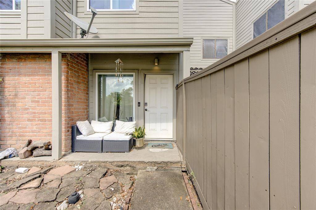 The inviting white door opens to a small patio area, perfect for relaxing with a morning coffee. A natural stone pathway winds through mature landscaping, adding character and a touch of nature to this serene outdoor space.