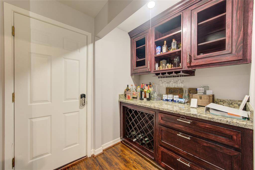 Featuring upper cabinets with sleek glass doors, a polished granite countertop, and a convenient wine rack below, this space is designed for effortless entertaining and sophisticated storage